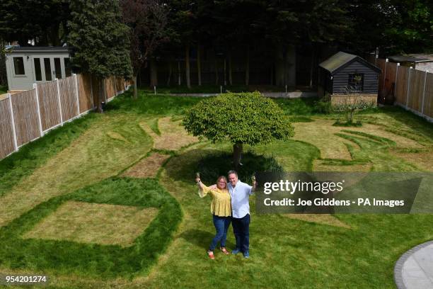 Sue Richards, 51 and 58-year-old Barry Maddox with their new lawn design of a giant champagne bottle and glasses, at their home in Billericay, Essex,...