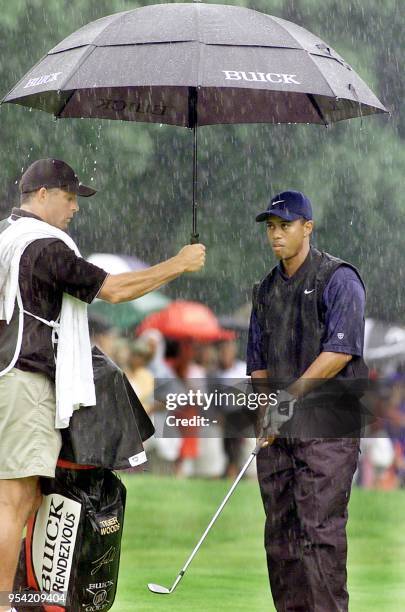 Tiger Woods prepares to chip onto the green on the 1st hole as his caddie Steve Williams holds his umbrella in the pouring rain during the 1st round...