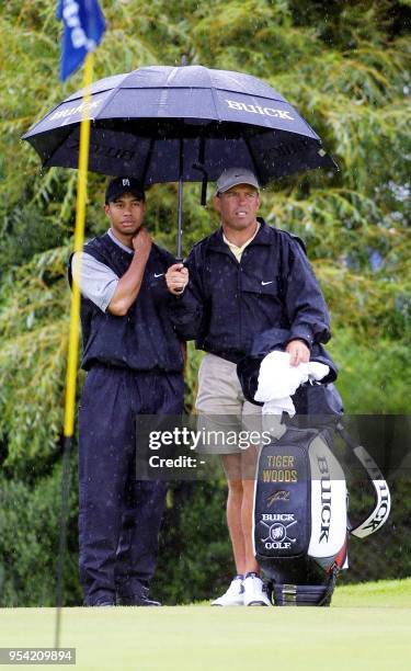 World Number one Tiger Woods with his caddie, New Zealander Steve Williams, shelters from the rain while keeping an eye on proceedings on the...