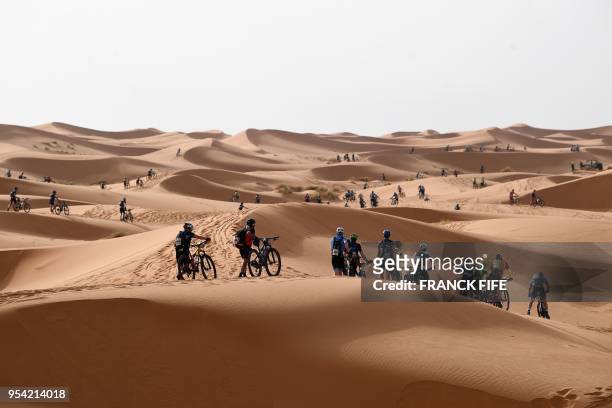 Competitors push their bikes along a sand dune during Stage 5 of the 13th edition of Titan Desert 2018 mountain biking race around Merzouga in...