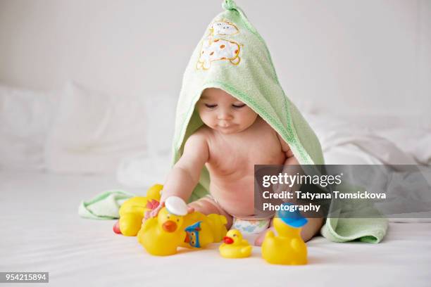 cute little baby toddler boy, playing with rubber ducks after bath in bed - baby bath toys stock pictures, royalty-free photos & images