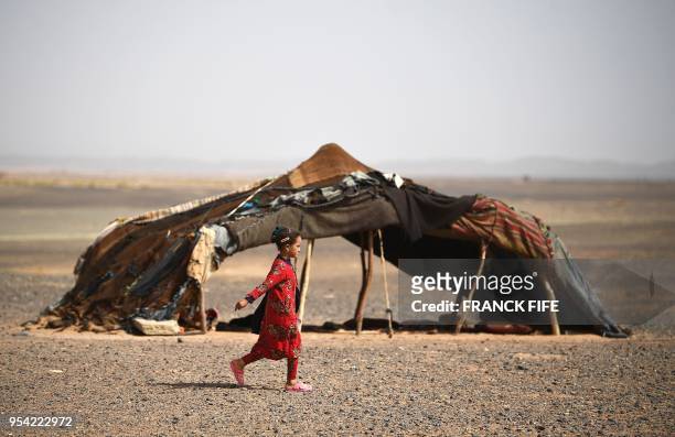 Moroccan girl walks past a tent during Stage 5 of the 13th edition of Titan Desert 2018 mountain biking race around Merzouga in Morocco on May 3,...