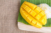 Thai style dessert, glutinious rice with mango on banana leaf and burlap background