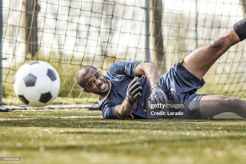 Young handsome soccer Goalkeeper diving and saving the ball during football training