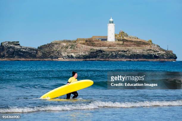 Young woman surfer in sea carrying surf board at godrevy, Cornwall, England, Britain, uk.