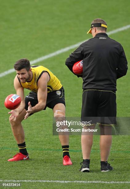 Trent Cotchin of the Tigers bends to catch the ball with a taped knee as Damien Hardwick, coach of the Tigers looks on during the Richmond Tigers AFL...