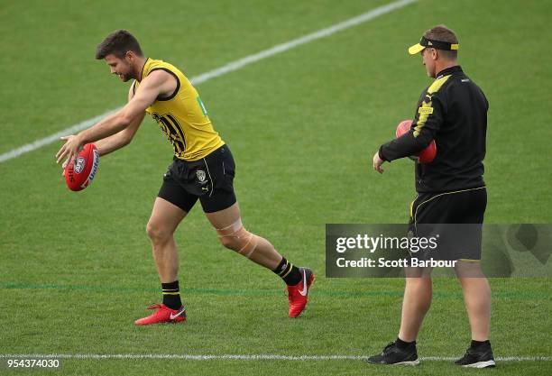 Trent Cotchin of the Tigers kicks the ball with a taped knee as Damien Hardwick, coach of the Tigers looks on during the Richmond Tigers AFL training...