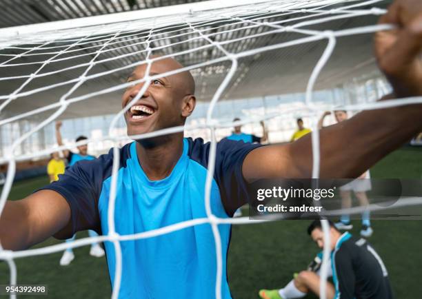 schwarze fußballer feiern, dass er nur ein tor hinter der fußballnetz suchen aufgeregt - hallenfußball wettbewerb stock-fotos und bilder