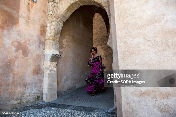 Girl wearing a typical flamenco dress walking throught the gate of Arco de las Pesas. El día de la Cruz or Día de las Cruces is one of the most...