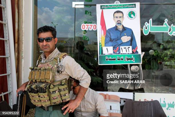 Private guard stands before a campaign poster for Rebwar Taha Mustafa, an Iraqi Kurdish member of the Iraqi federal parliament and a Patriotic Union...