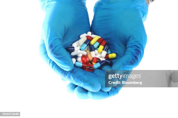 Hands wearing blue surgical gloves hold brightly coloured pharmaceutical medication, including antibiotics, paracetamol, Ibuprofen and cold relief...