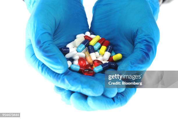 Hands wearing blue surgical gloves hold brightly coloured pharmaceutical medication, including antibiotics, paracetamol, Ibuprofen and cold relief...