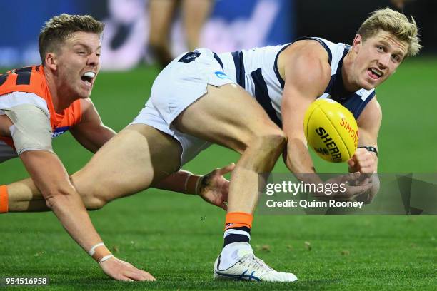 Scott Selwood of the Cats handballs whilst being tackled by Aidan Corr of the Giants during the round seven AFL match between the Geelong Cats and...