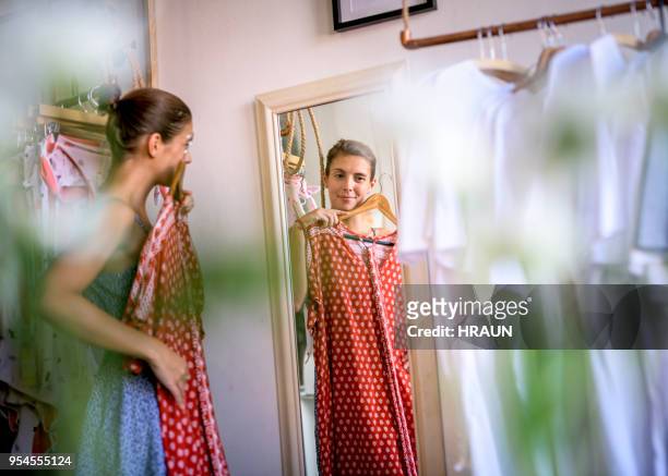 donna che si guarda allo specchio mentre prova a vestirsi in camera in un negozio. - vestito da donna foto e immagini stock