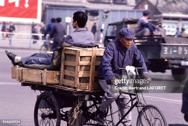 Un homme sur son vélo tractant une remorque sur laquelle un homme est assis en novembre 1981, Chine.