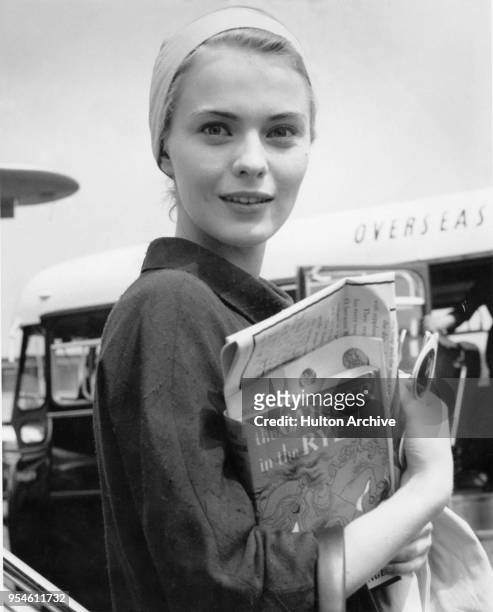 American actress Jean Seberg arrives at an airport carrying a copy of the book 'The Catcher in the Rye' by J. D. Salinger, 1957.