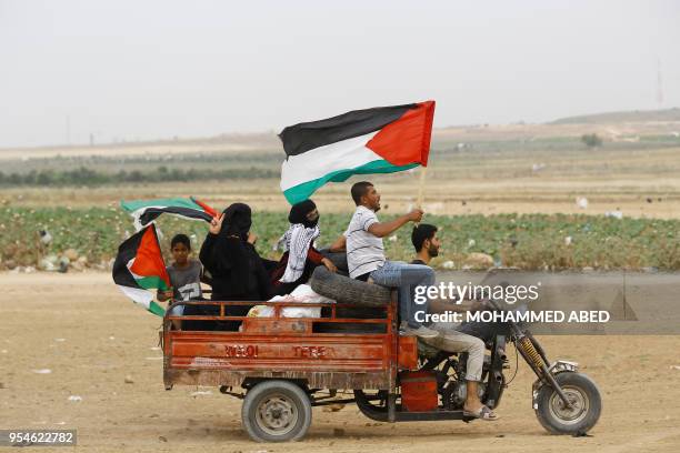 Palestinian protesters wave national flags as they transport tyres on a motorcycle car to burn them during protests near the border fence between...