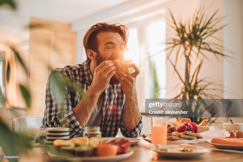 Bebaarde man met een boterham voor ontbijt thuis.