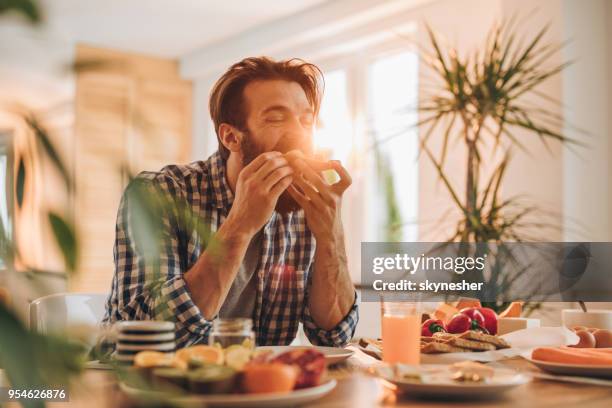 bearded man having a sandwich for breakfast at home. - eat man stock pictures, royalty-free photos & images