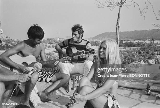 Brigitte Bardot écoute Philippe Debarge et Johnny Hallyday jouer de la guitare à l'Epi-Plage en août 1967 à Saint-Tropez, France.