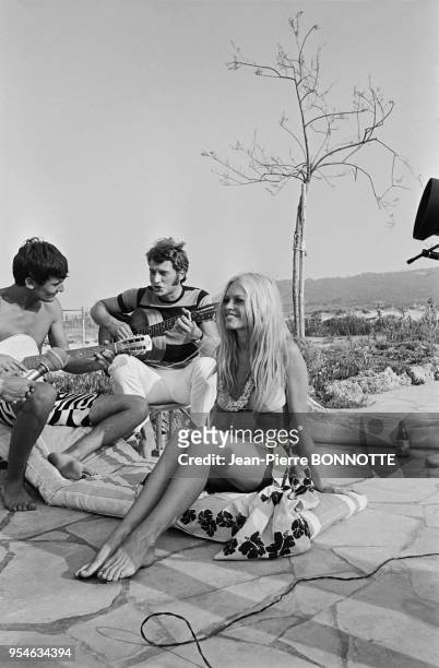 Brigitte Bardot écoute Philippe Debarge et Johnny Hallyday jouer de la guitare à l'Epi-Plage en août 1967 à Saint-Tropez, France.