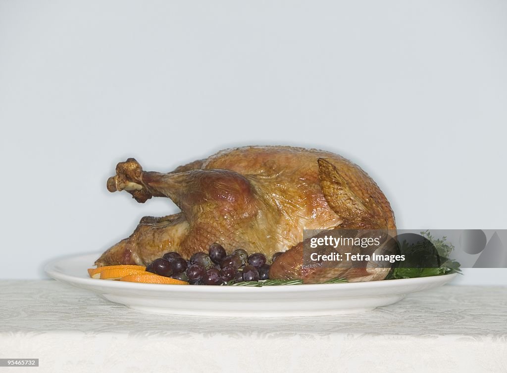 A roasted chicken on a plate with garnishes