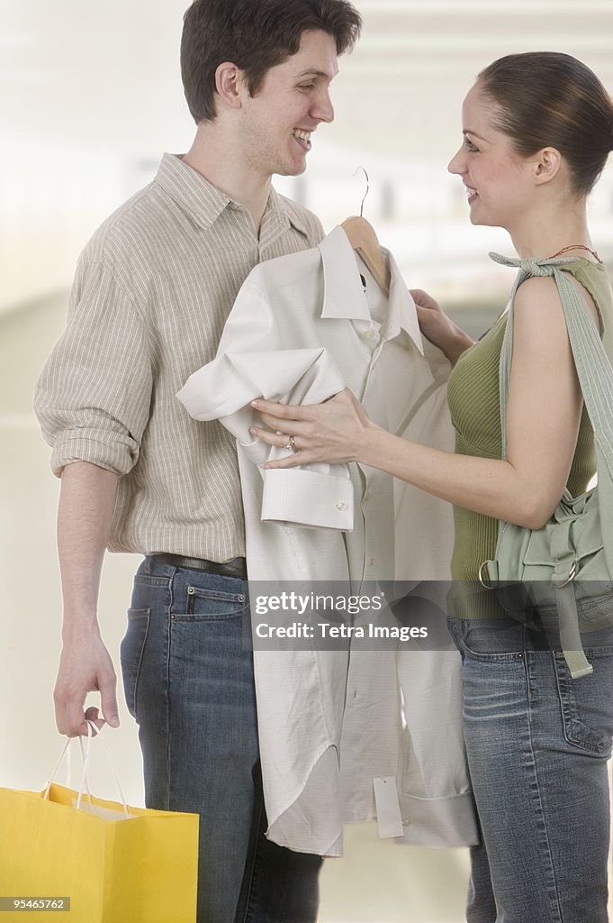 A young woman holding up a shirt to a young man while shopping