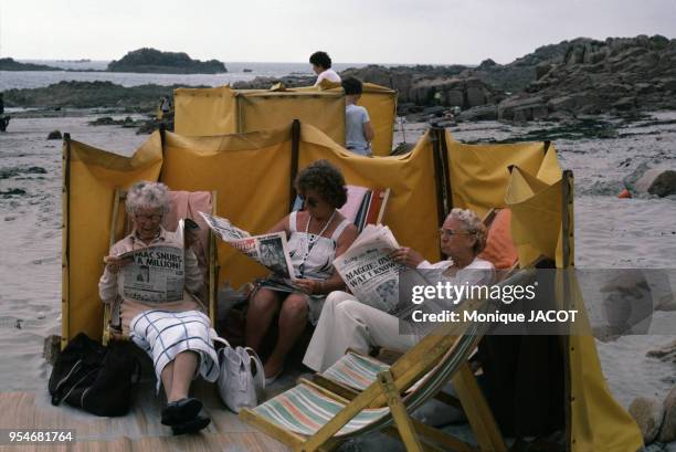 Femmes âgées lisant le journal sur la plage sur l'île de Guernesey, en août 1985, Royaume-Uni.