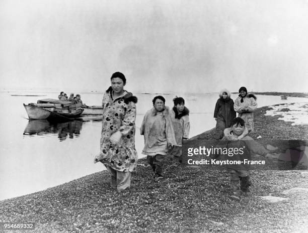 Femmes et enfants esquimaux remorquant une barque chargée des murs de leur maison faits de caisses jetées par les Blancs, à Point Barrow en Alaska,...