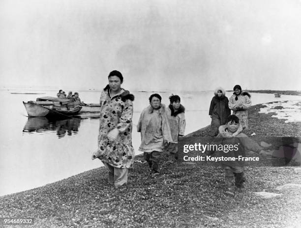 Femmes et enfants esquimaux remorquant une barque chargée des murs de leur maison faits de caisses jetées par les Blancs, à Point Barrow en Alaska,...