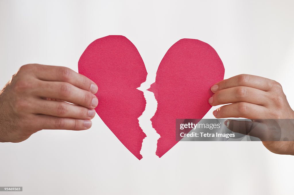 Two hands holding broken paper heart
