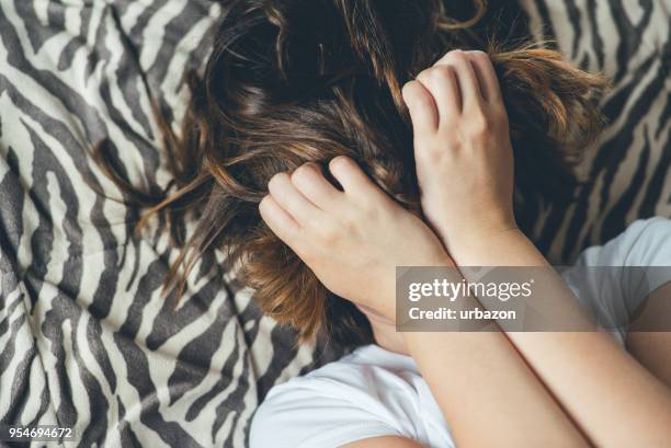 woman lies on a bed with hands across her face. - embarrassment stock pictures, royalty-free photos & images