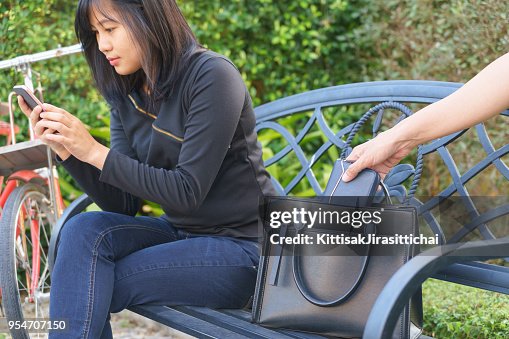 Thief trying to steal and walk away the wallet while woman using mobile phone and sitting on chair Thief trying to steal and walk away the wallet while woman using mobile phone and sitting on chair