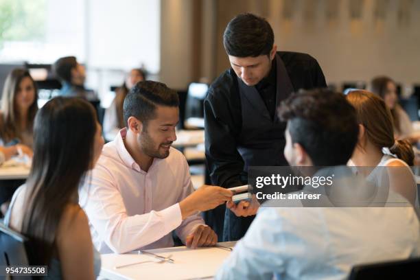 handsome man paying the waiter with his smartphone at the restaurant looking very happy - paying for dinner imagens e fotografias de stock