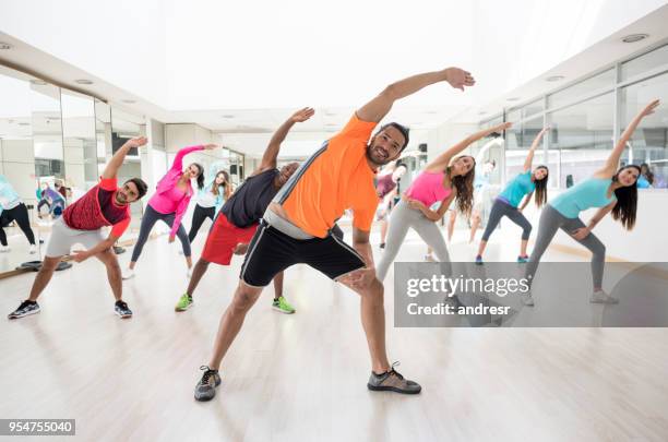 cheerful instructor guiding his class to strecth at the gym - aeróbica imagens e fotografias de stock