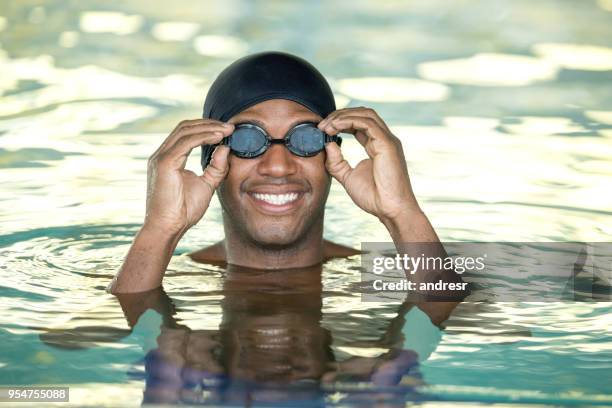 black cheerful young man putting on the swimming goggles looking at camera very happy at the pool - indoor swimming pool stock pictures, royalty-free photos & images