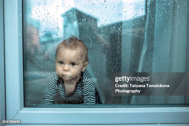 cute toddler boy, staying at home behind the glass doors or window, watching outside"n - hinterhaus stock-fotos und bilder