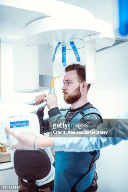 young man taking 3d panoramic digital x-ray of his teeth - tomography stock pictures, royalty-free photos & images