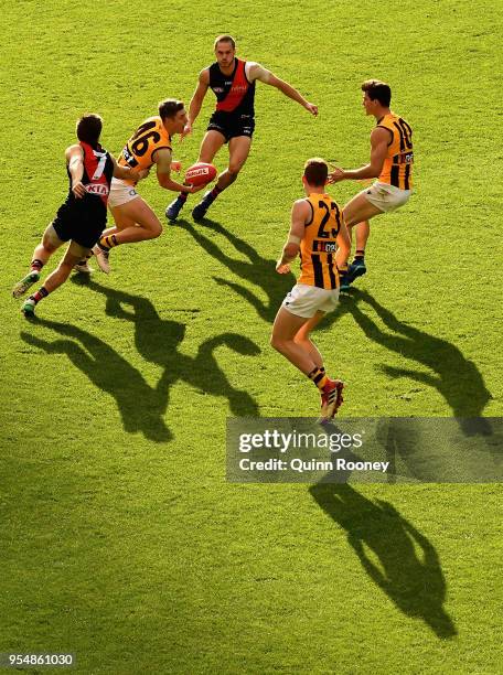 James Cousins of the Hawks handballs whilst being tackled by Zach Merrett of the Bombers during the round seven AFL match between the Essendon...