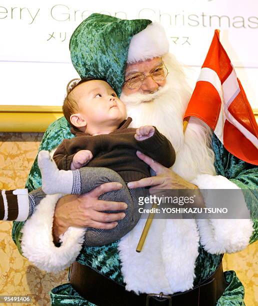Man dreesed in a green Santa Claus suit carries a Danish flag as he holds a Japanese boy at the Mitsukoshi department store in Tokyo on December 5,...
