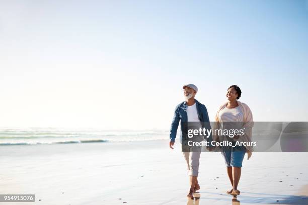 crogiolarsi nei raggi di un felice pensionamento - couple walking on beach foto e immagini stock