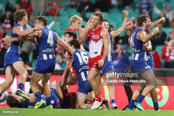 Kangaroos players celebrate victory as Luke Parker of the Swans looks dejected after the round seven AFL match between the Sydney Swans and the North...