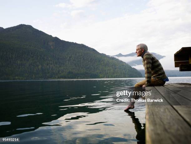 man sitting on edge of dock with feet in water - ponton photos et images de collection