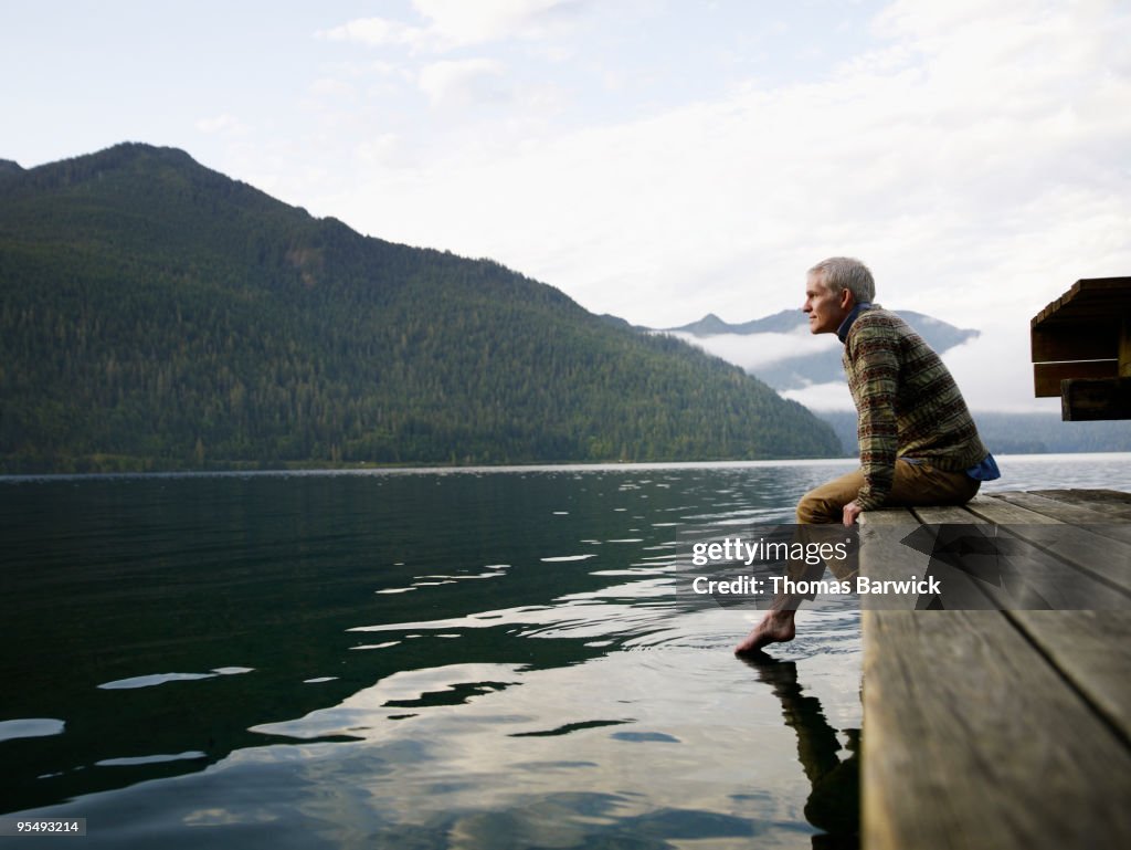 Man sitting on edge of dock with feet in water