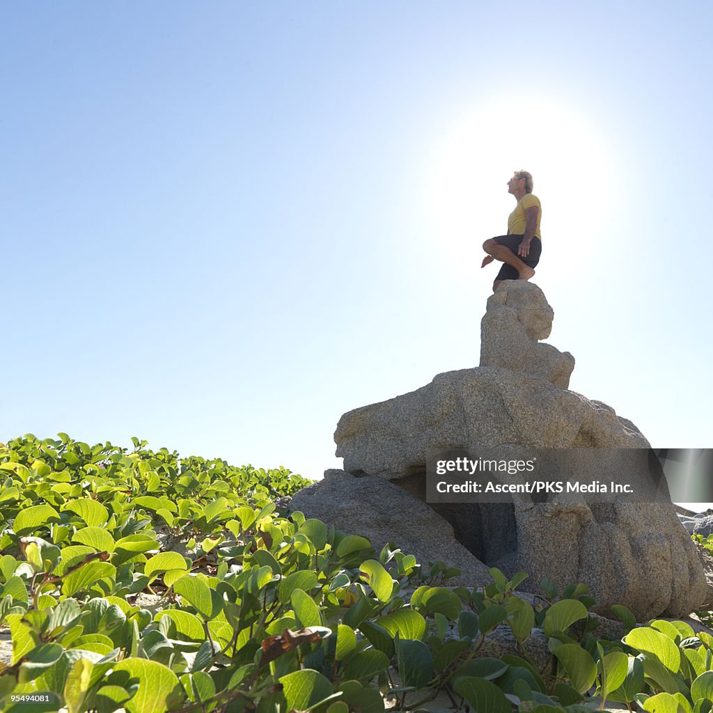 Man stands on top of pinnacle above greenery