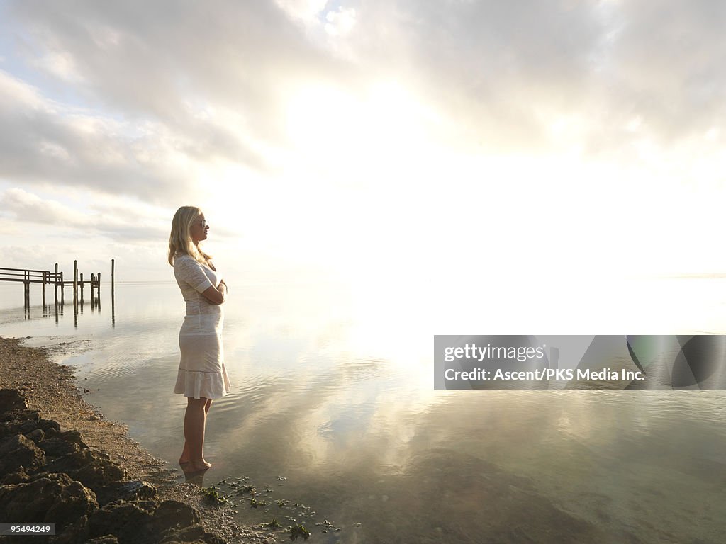 Woman watches sunrise over shimmering sea, pier