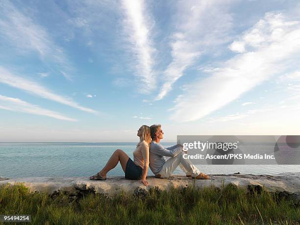 couple sit on rocks above sea, facing opposite way - back to back stockfoto's en -beelden