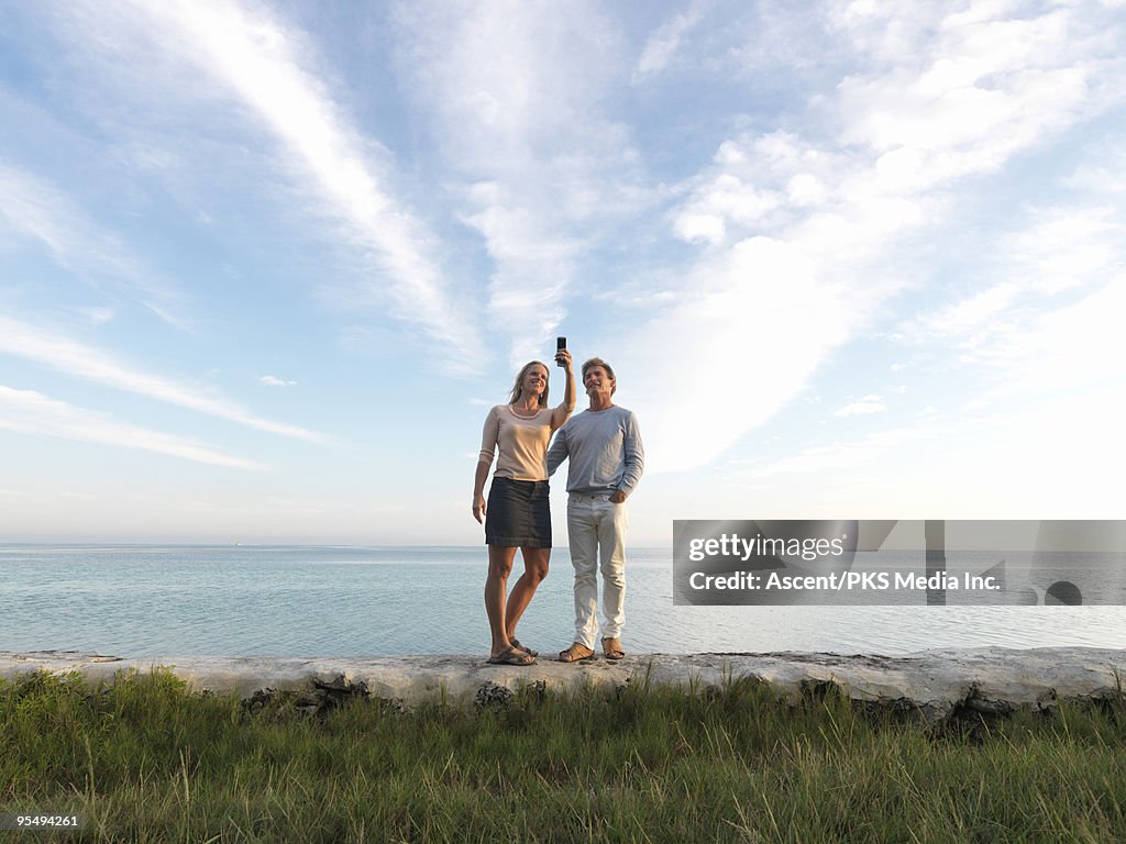 Couple stand on rocks above sea, snap cell picture