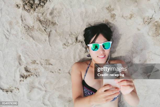mujer escuchando música en la playa - sunglasses overhead fotografías e imágenes de stock