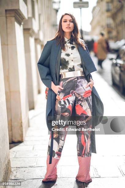 Landiana Cerciu wears a white shirt with black patterns ; a petrol-blue round-edges kimono-style coat ; a golden belt ; a red shoulder-bag with...